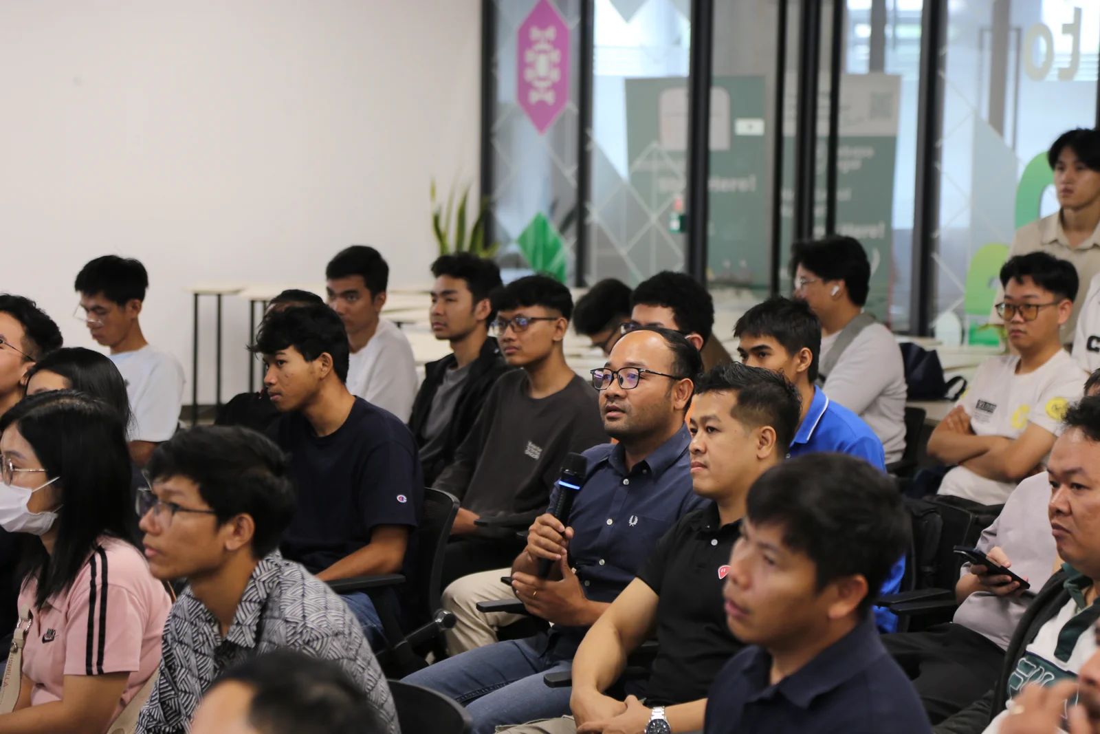 An attendee speaking into a microphone among rows of participants at the Cambodia meetup.